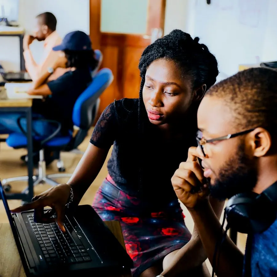 Two developers pairing on a change at a laptop in an open office